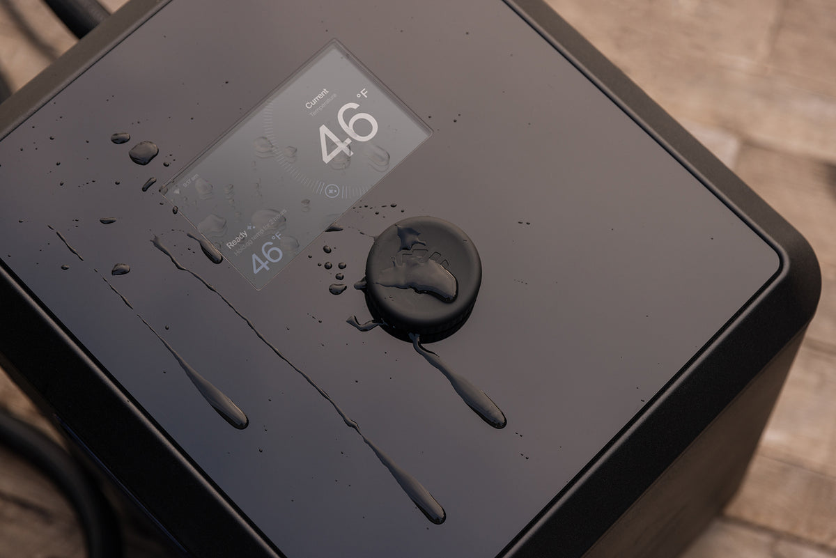 A close-up of a black smart water chiller with a digital display screen showing 46°F and a circular power button, with water droplets on its surface.